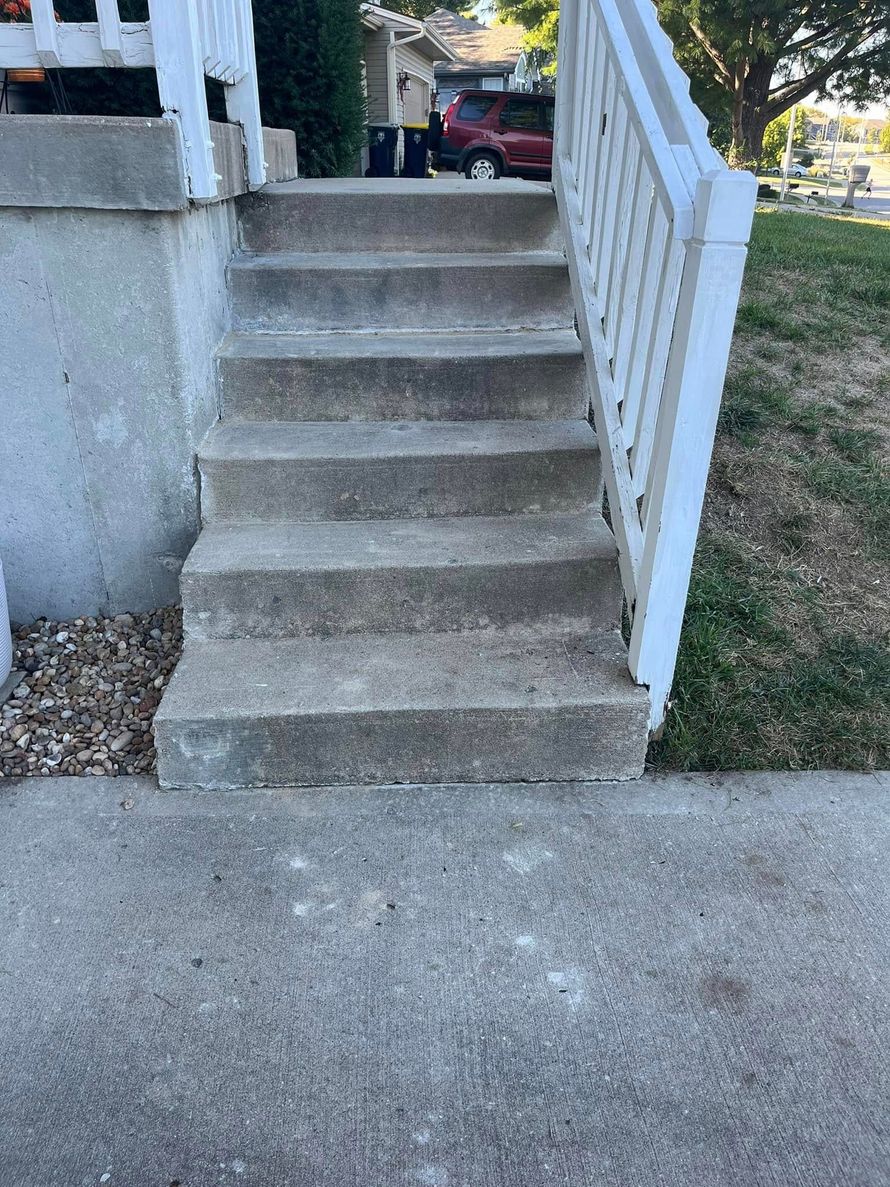 Concrete front steps with a white handrail leading up to a porch.