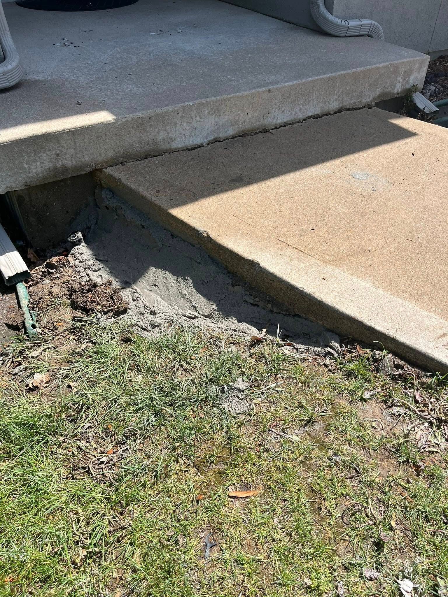 Broken concrete porch step with cracked ramp and uneven edge beside a patchy grass yard