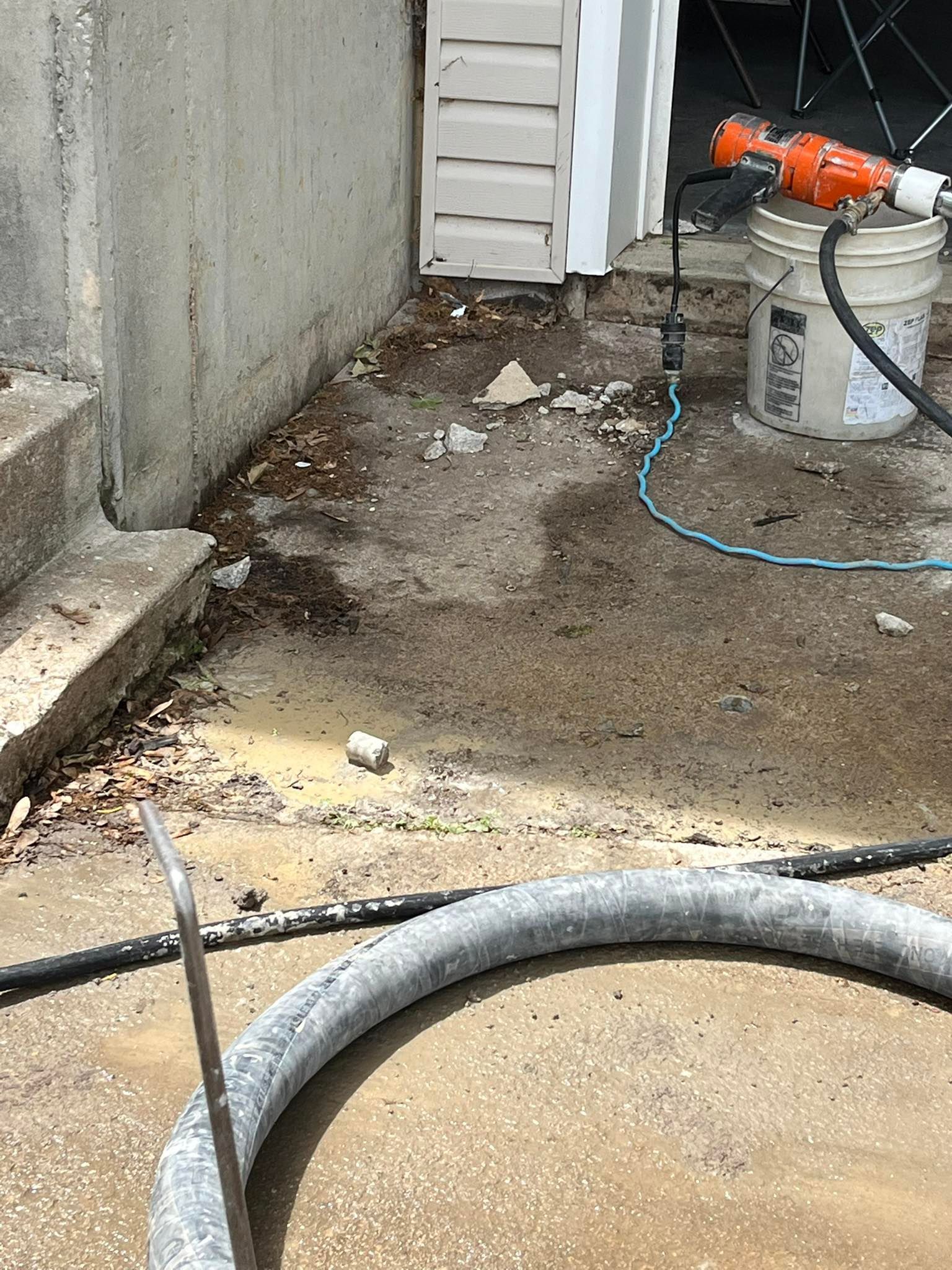 Construction work area with wet concrete, hose, and orange pump beside a wall