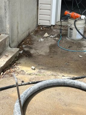 Concrete area with dirt and debris, a hose, and an orange power tool near a wall