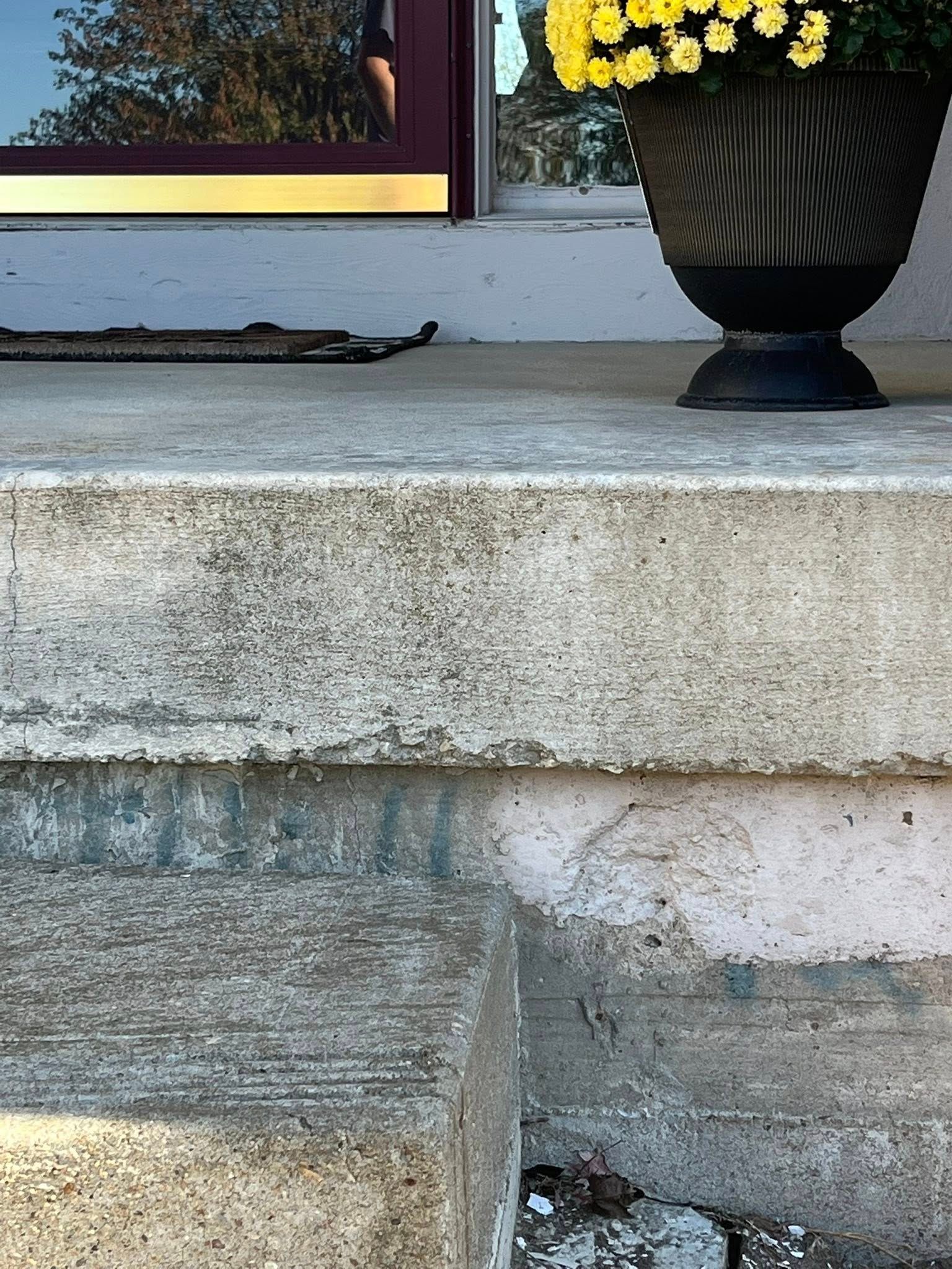 Concrete steps with a black vase of yellow flowers on a porch ledge