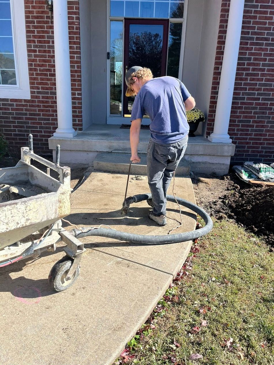 Worker vacuuming debris from a concrete walkway outside a brick house