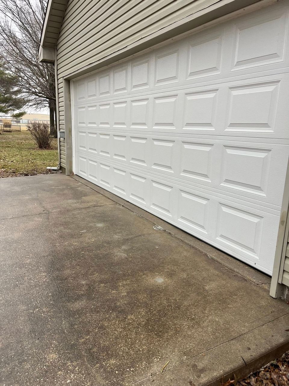 White garage door on a concrete driveway beside a beige house.