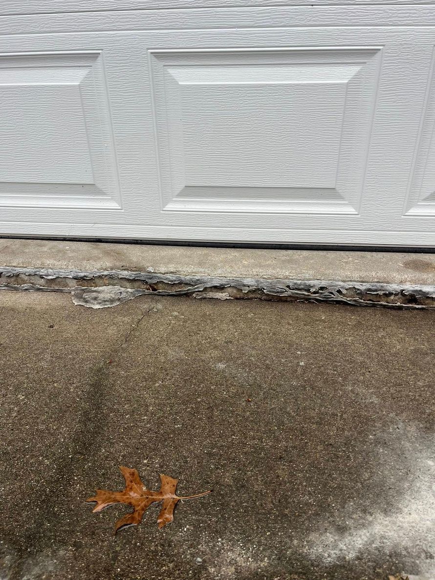 Concrete driveway with a white garage door and a small orange leaf on the wet pavement