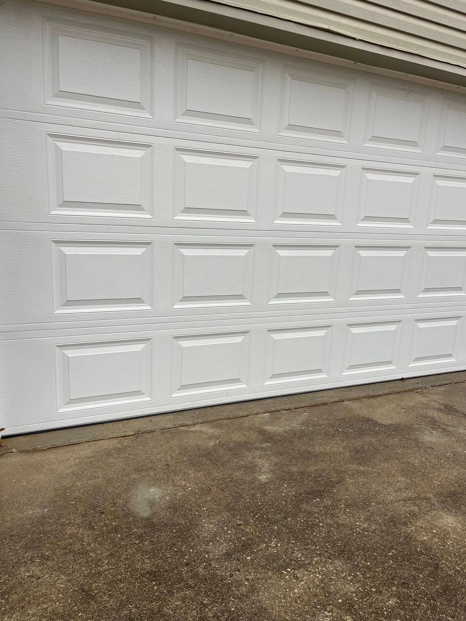 White textured garage door with rectangular panels beside a gravel driveway