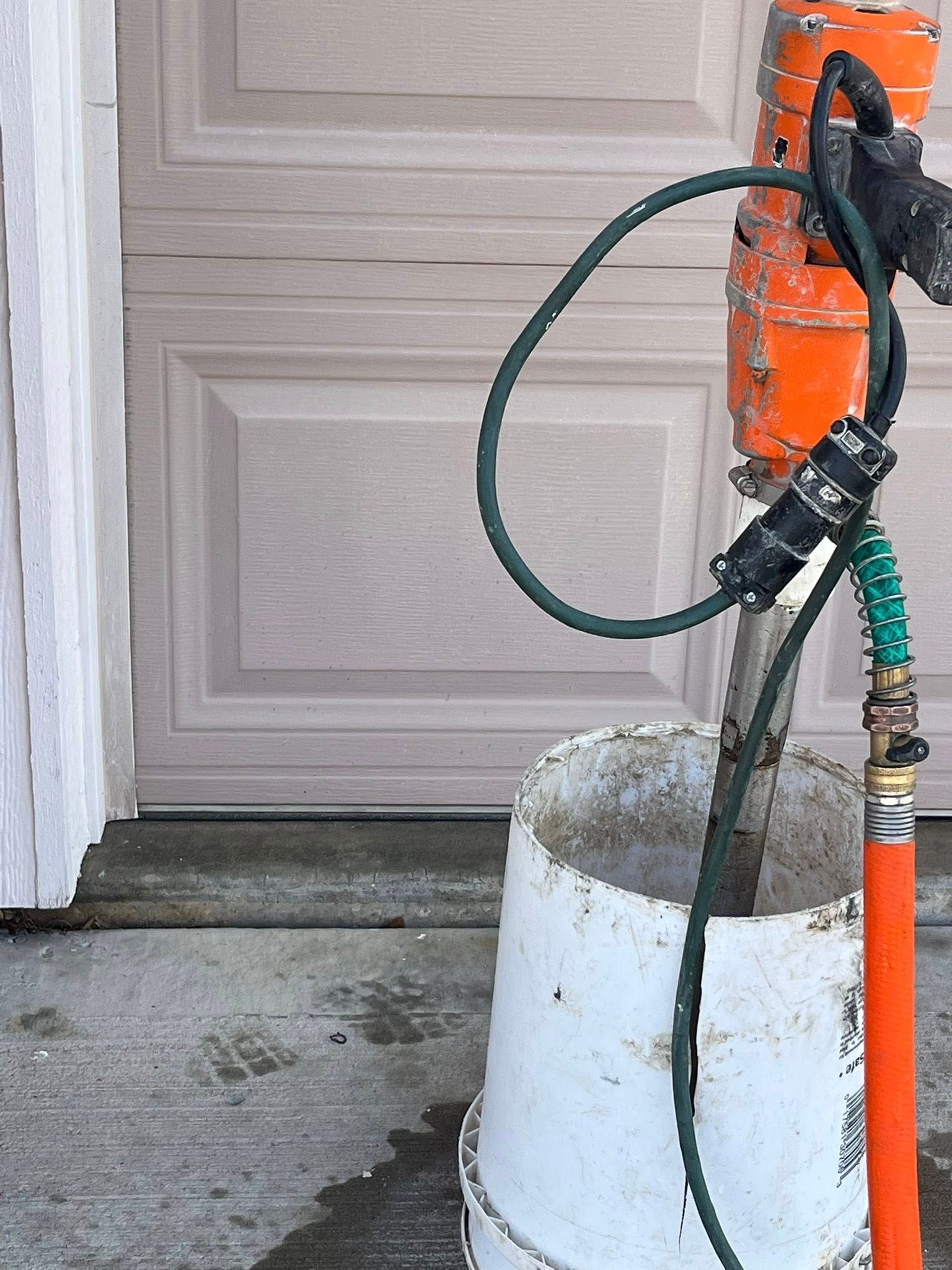 Orange pressure washer beside a garage door, with hose coiled around a white bucket.