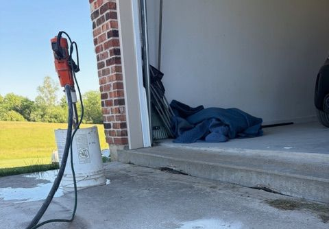 Garage interior with a red power tool, folded blue tarp, and open doorway to a grassy yard.