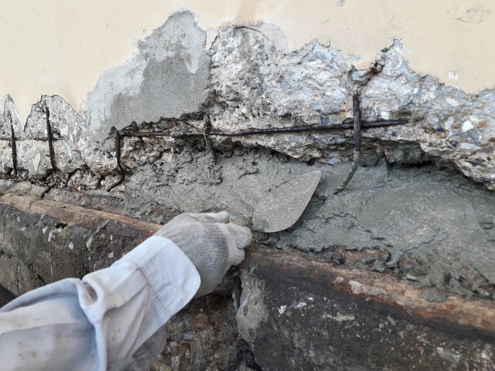 Hand wearing a white glove spreads mortar over a cracked wall during repair work
