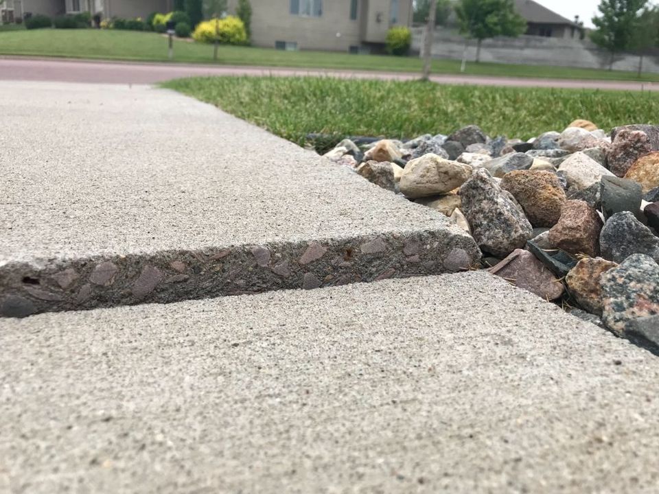 Cracked concrete sidewalk beside a decorative rock border in a suburban yard