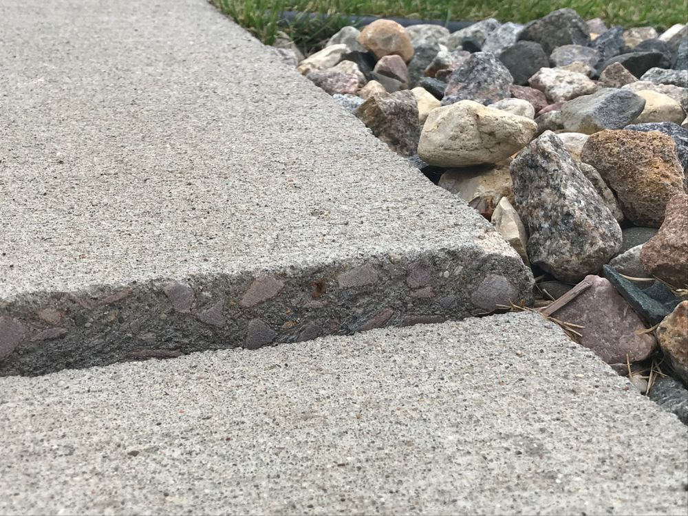 Broken concrete sidewalk with a cracked step beside a gravel rock bed.