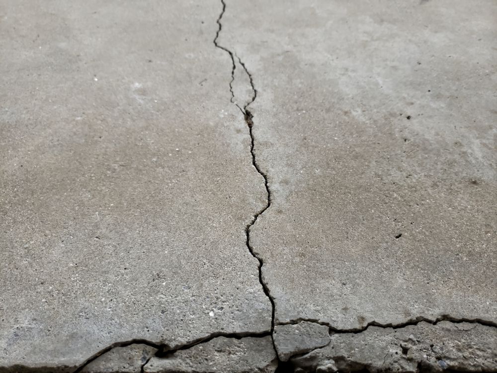 Cracked concrete surface with a long vertical crack and horizontal fracture near the bottom