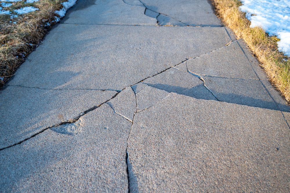 Cracked concrete sidewalk with large broken sections and gaps along the edges