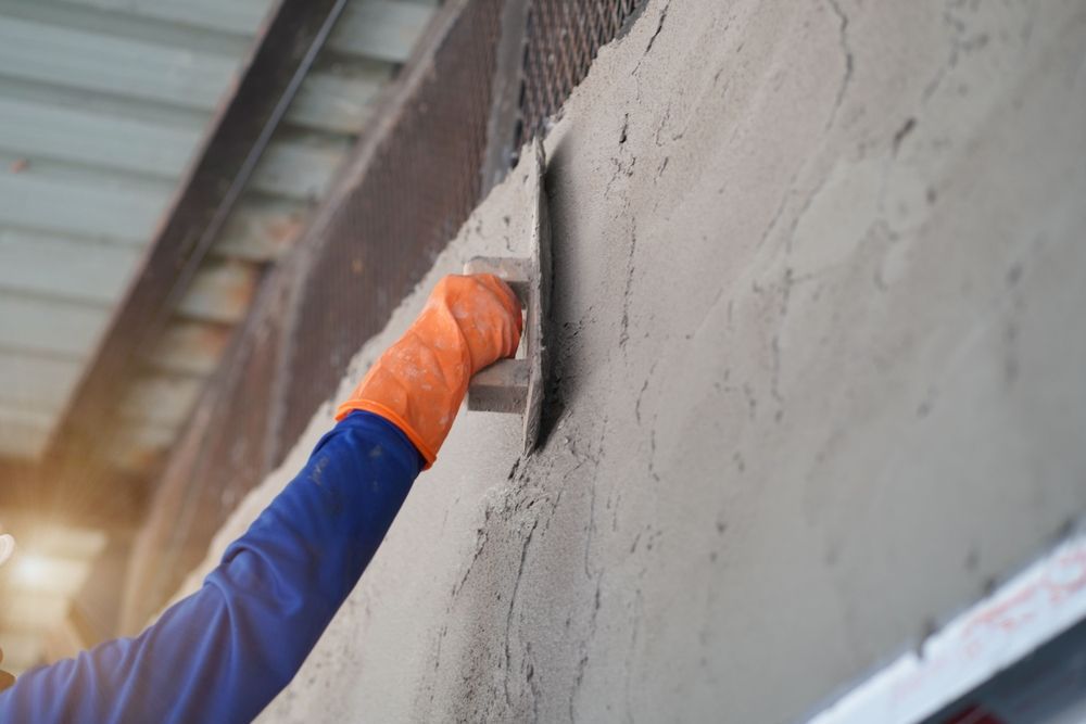 Worker in orange gloves smoothing wet concrete on a wall with a trowel.