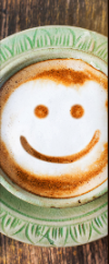 Smiley face drawn in coffee foam on a white cup with a green rim