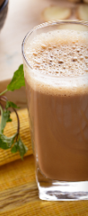 Tall glass of frothy beige drink on a wooden table with a blurred green plant in the background
