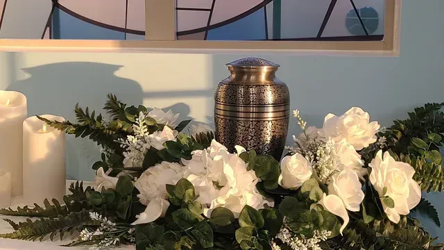 White flowers and greenery arranged around a silver urn and candles on a windowsill.