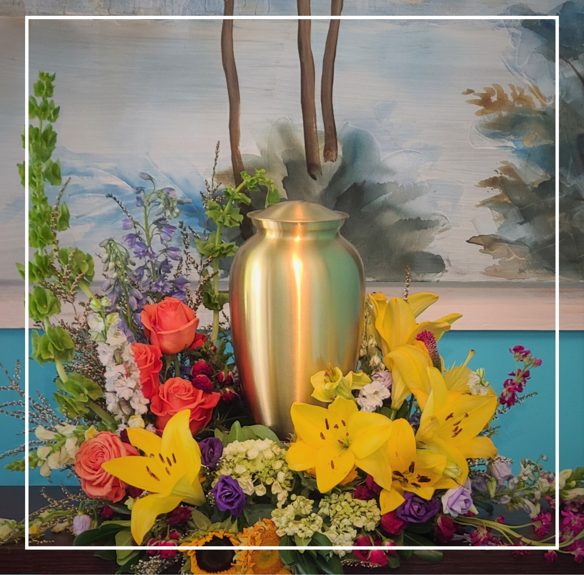 Colorful floral arrangement with yellow lilies and a gold vase against a painted backdrop