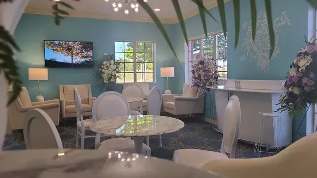 Elegant lounge with teal walls, white chairs, round tables, lamps, and large windows