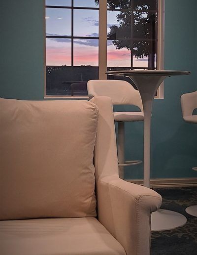 Living room with beige chair, white bar stools, and a sunset view through a window