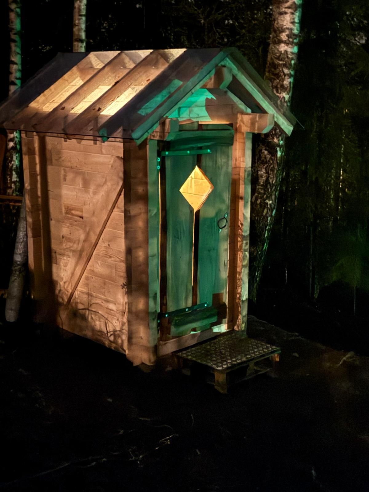 Valaistu Hiisi PuuCee -kompostikäymälä koirametsässä illalla