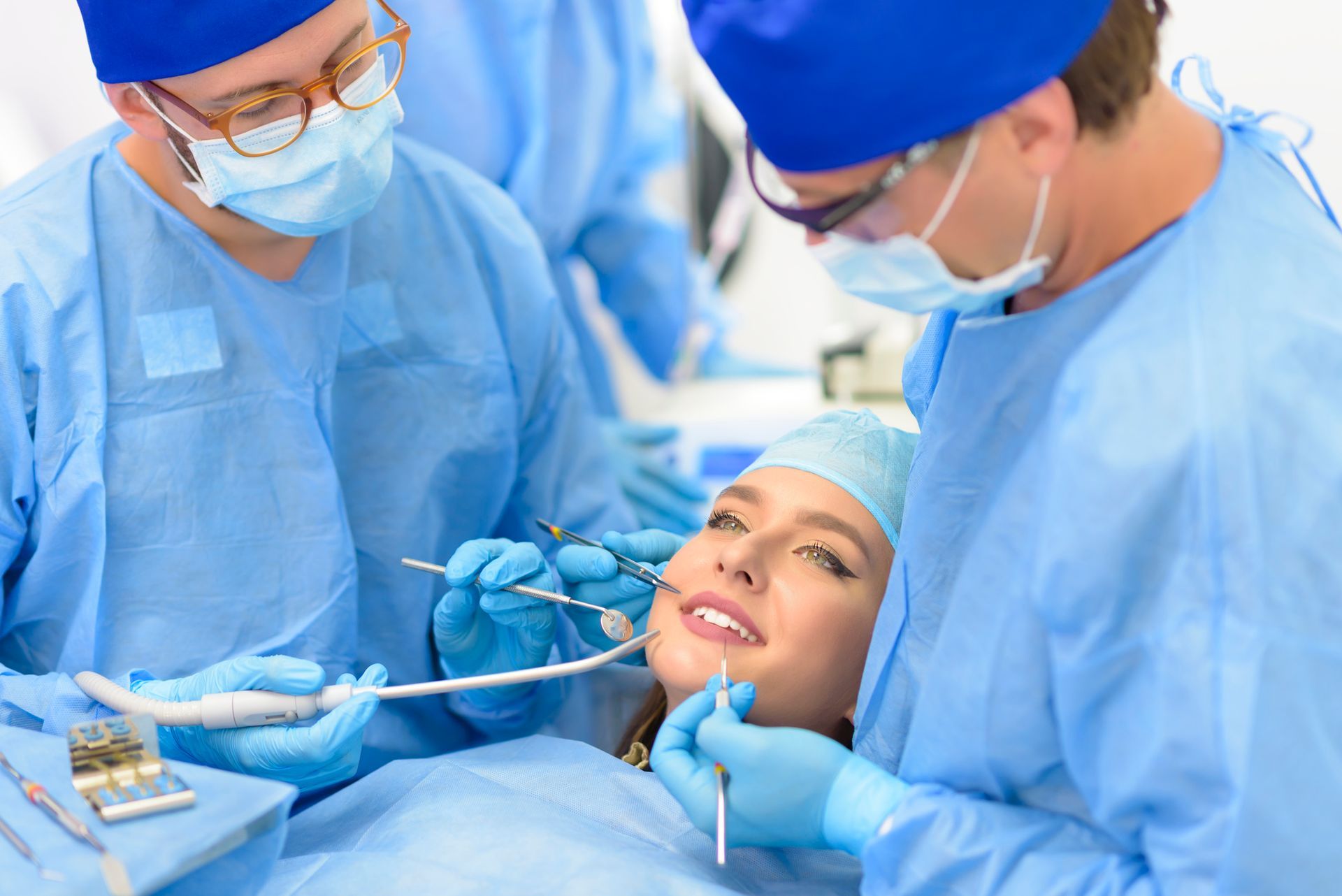 Due chirurghi eseguono un intervento odontoiatrico su una donna sorridente in una clinica, tutti e due indossando la divisa chirurgica blu.