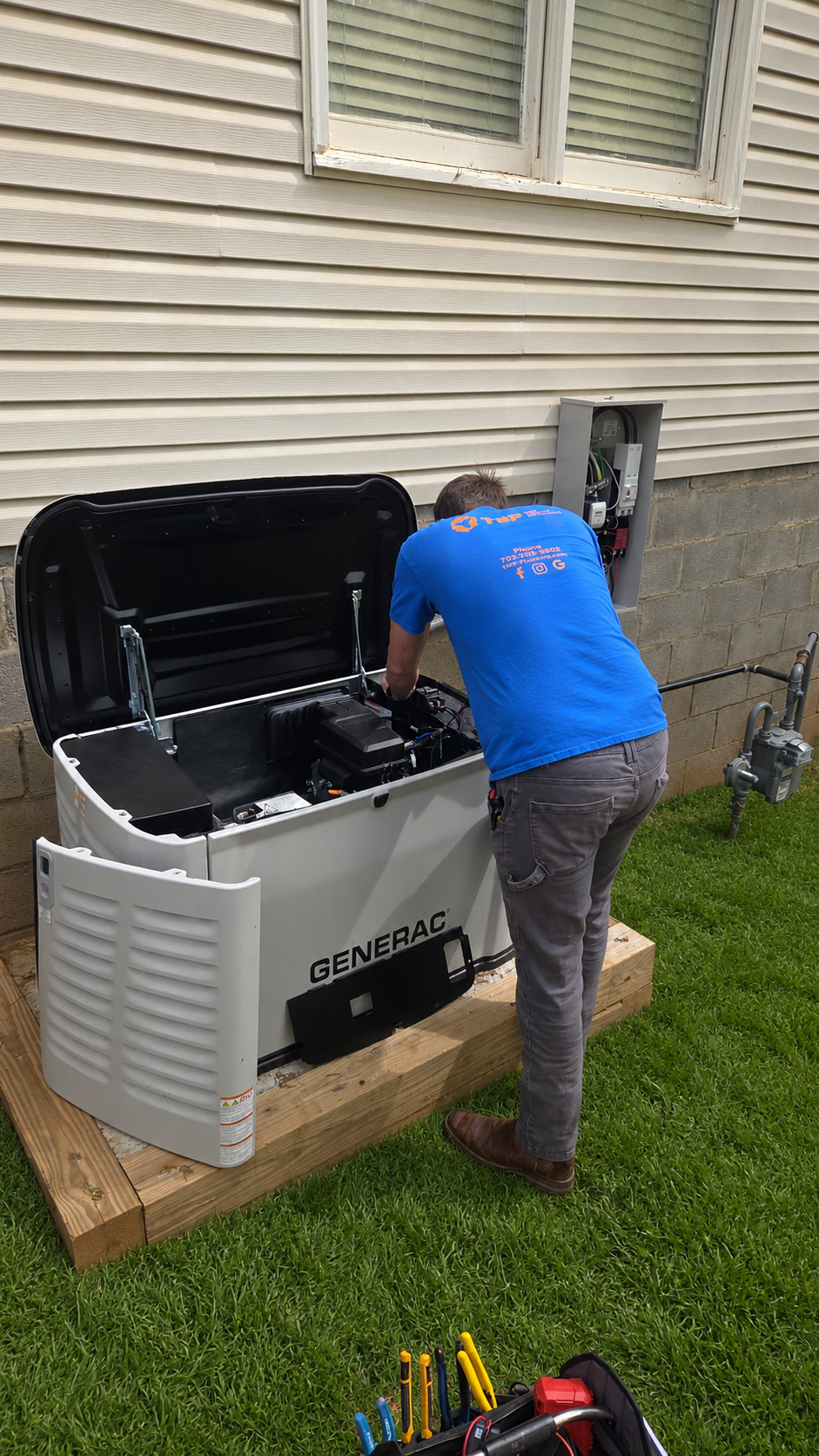 Person working on an outdoor portable heater next to a house, with tools on the grass.