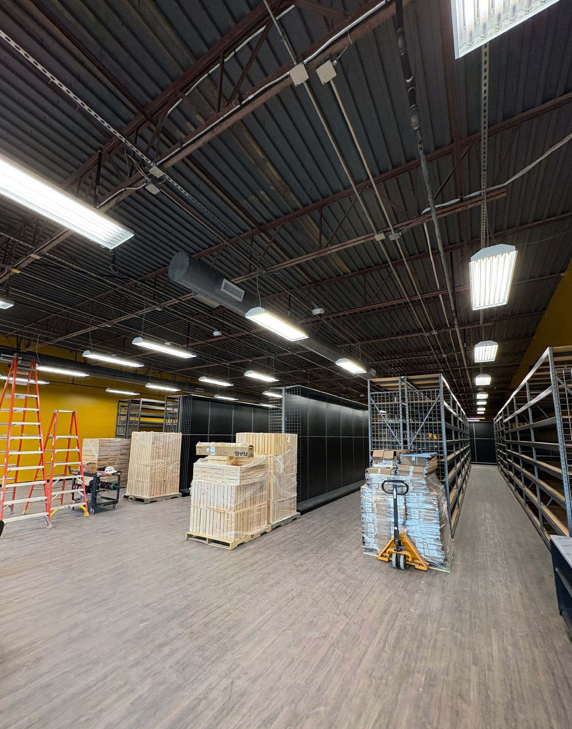 Warehouse aisle with stacked pallets and shelving under bright overhead lights