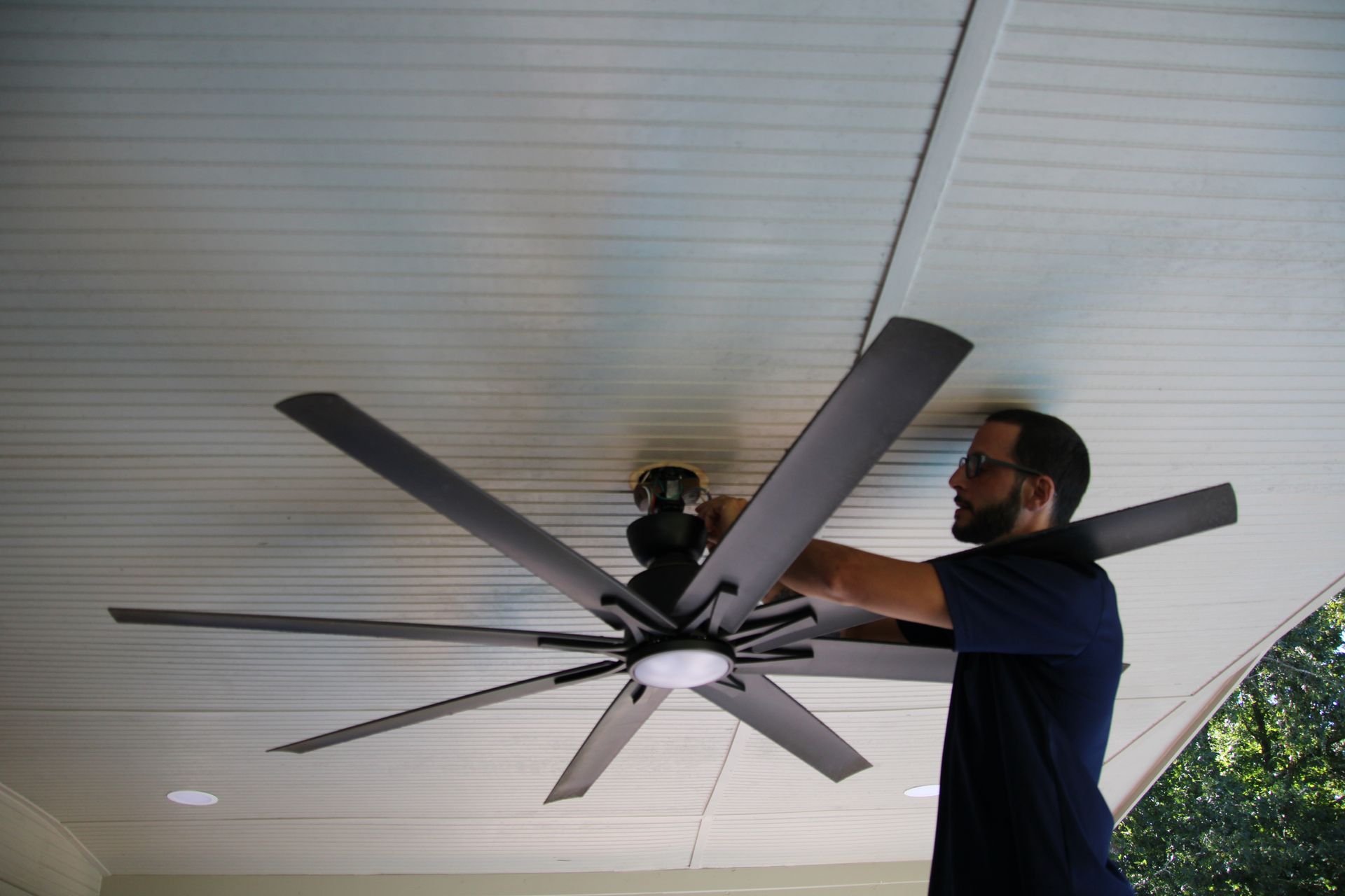 Man installing a large ceiling fan on a covered porch ceiling