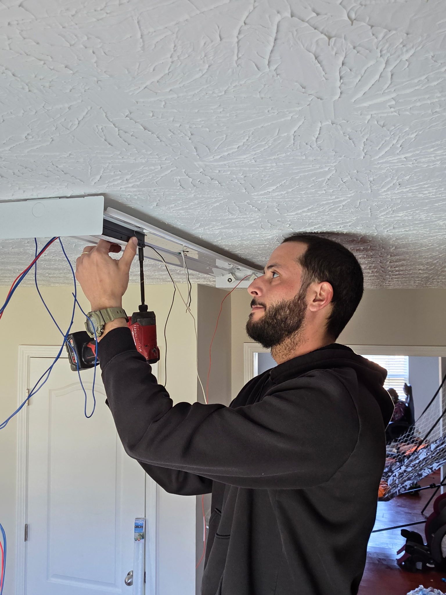 Man adjusting a garage door opener on a ceiling-mounted track, with tools and wires visible.