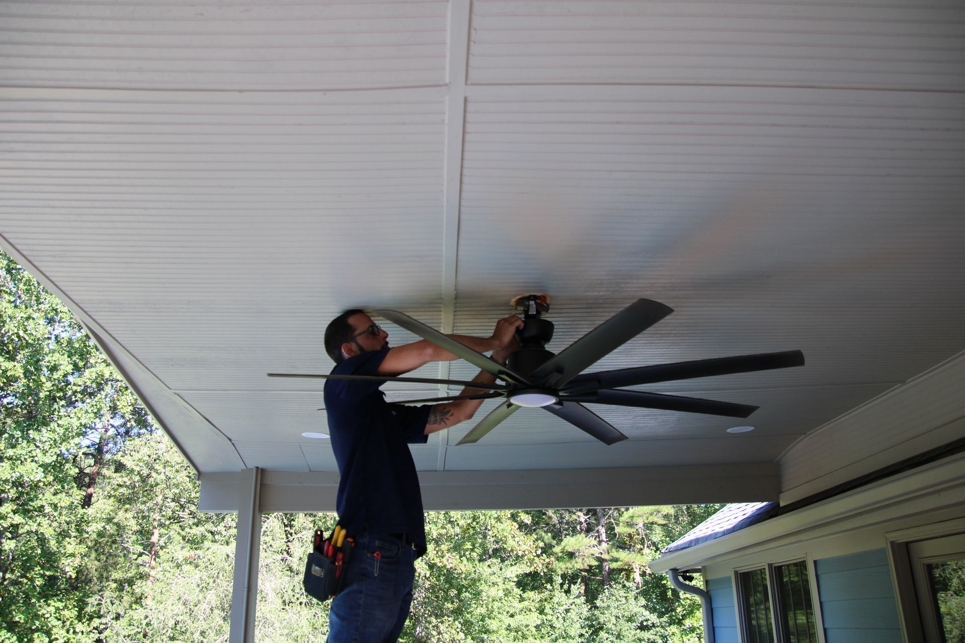 Person installing a ceiling fan on a covered porch, using a power drill