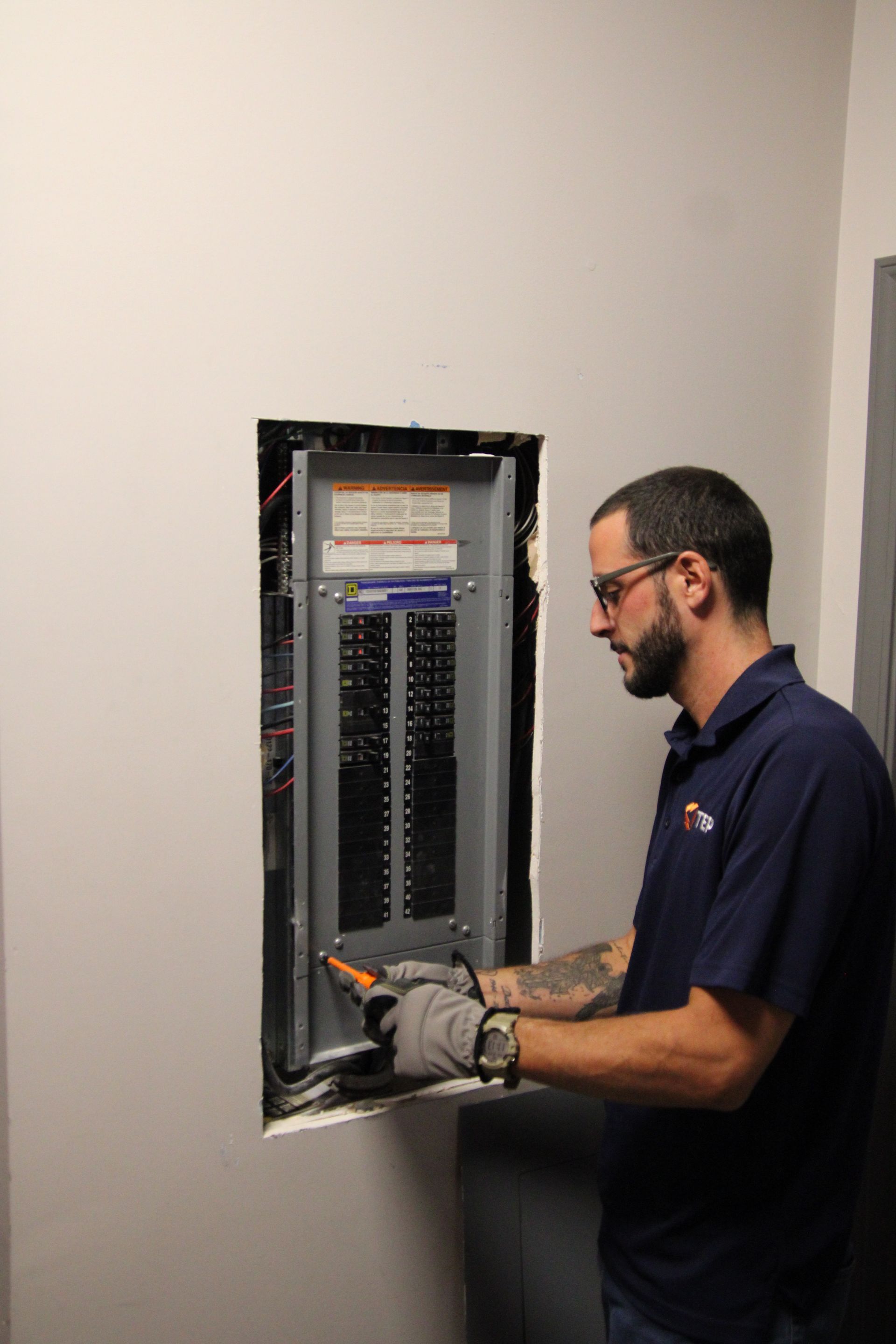 Technician working inside an open electrical breaker panel with tools