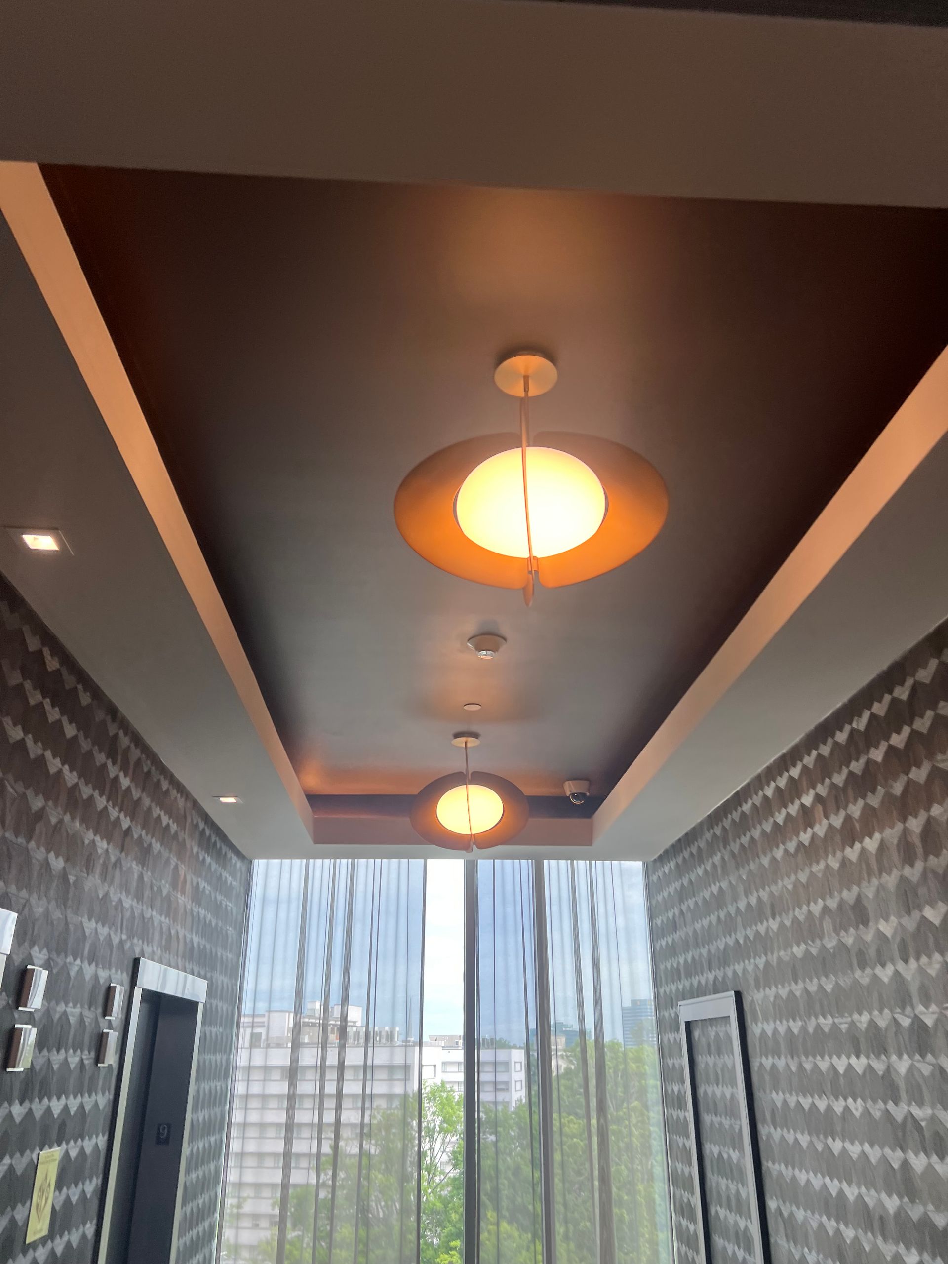 Modern hallway with dark ceiling lights, patterned walls, and a bright window view of city buildings and trees.
