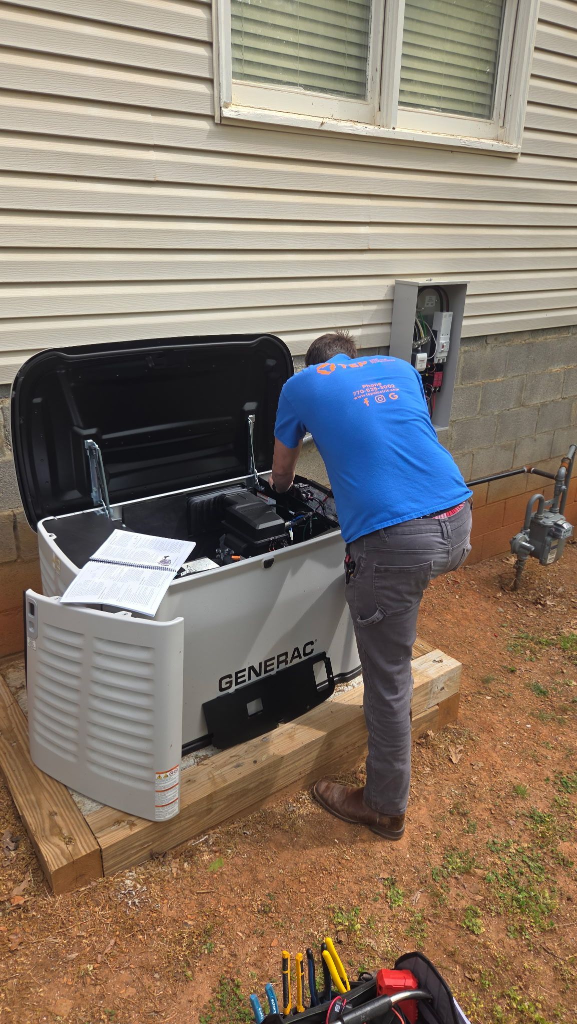 Person in blue shirt working on an open outdoor grill beside a house.