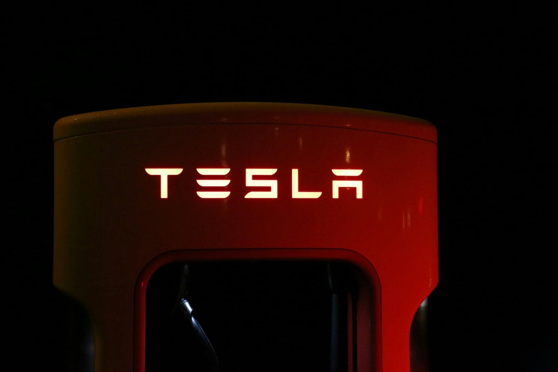 Illuminated Tesla Supercharger with red casing and the logo glowing in white.