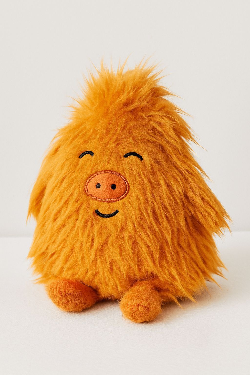Oranje, pluizig pluche speeltje met een lachend gezichtje, een varkensneusje en kleine voetjes.