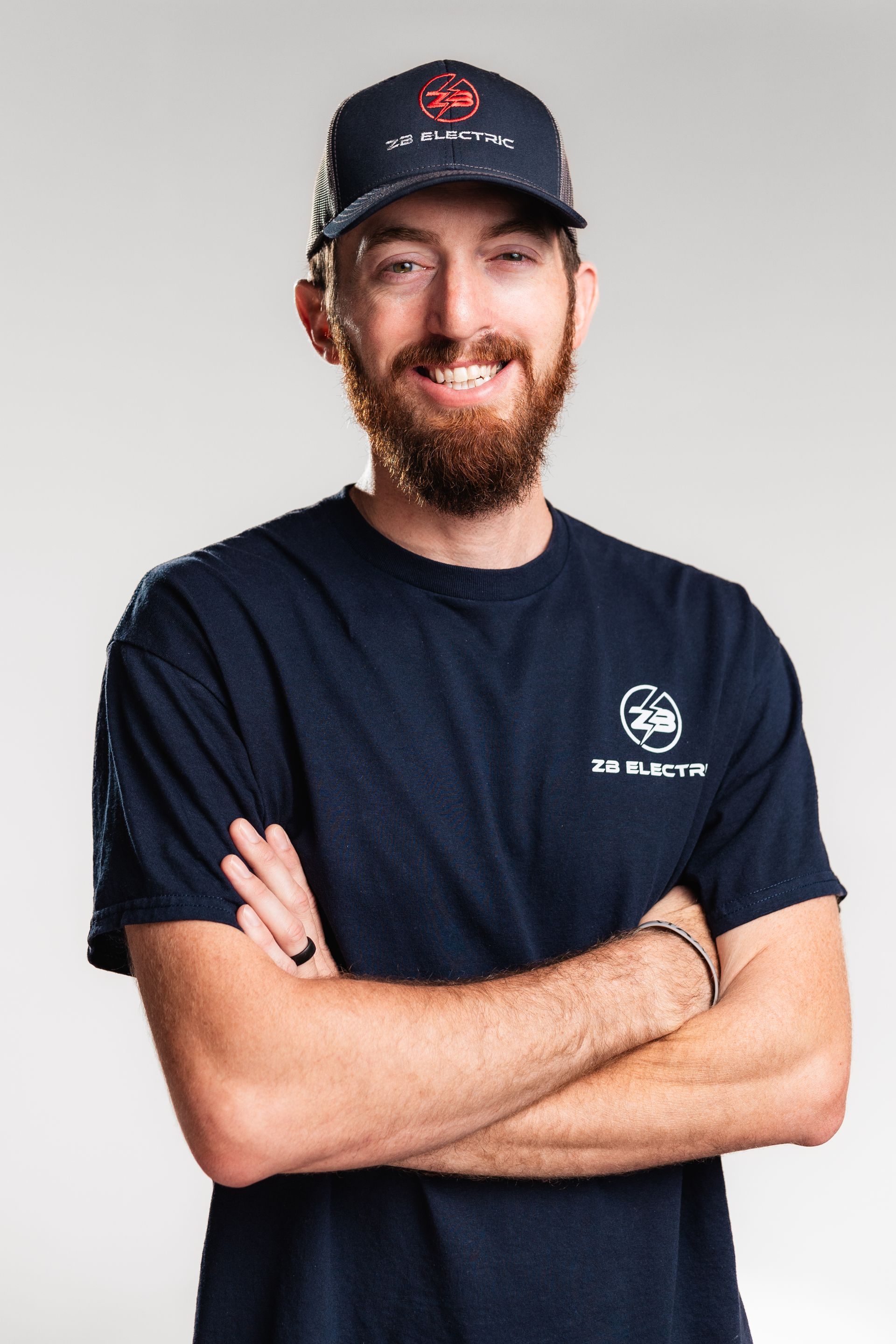 A man with a beard and a hat is standing with his arms crossed.