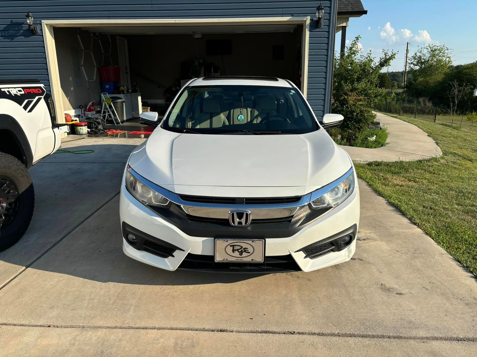 A white honda civic is parked in front of a garage. A white honda civic is parked in front of a garage.