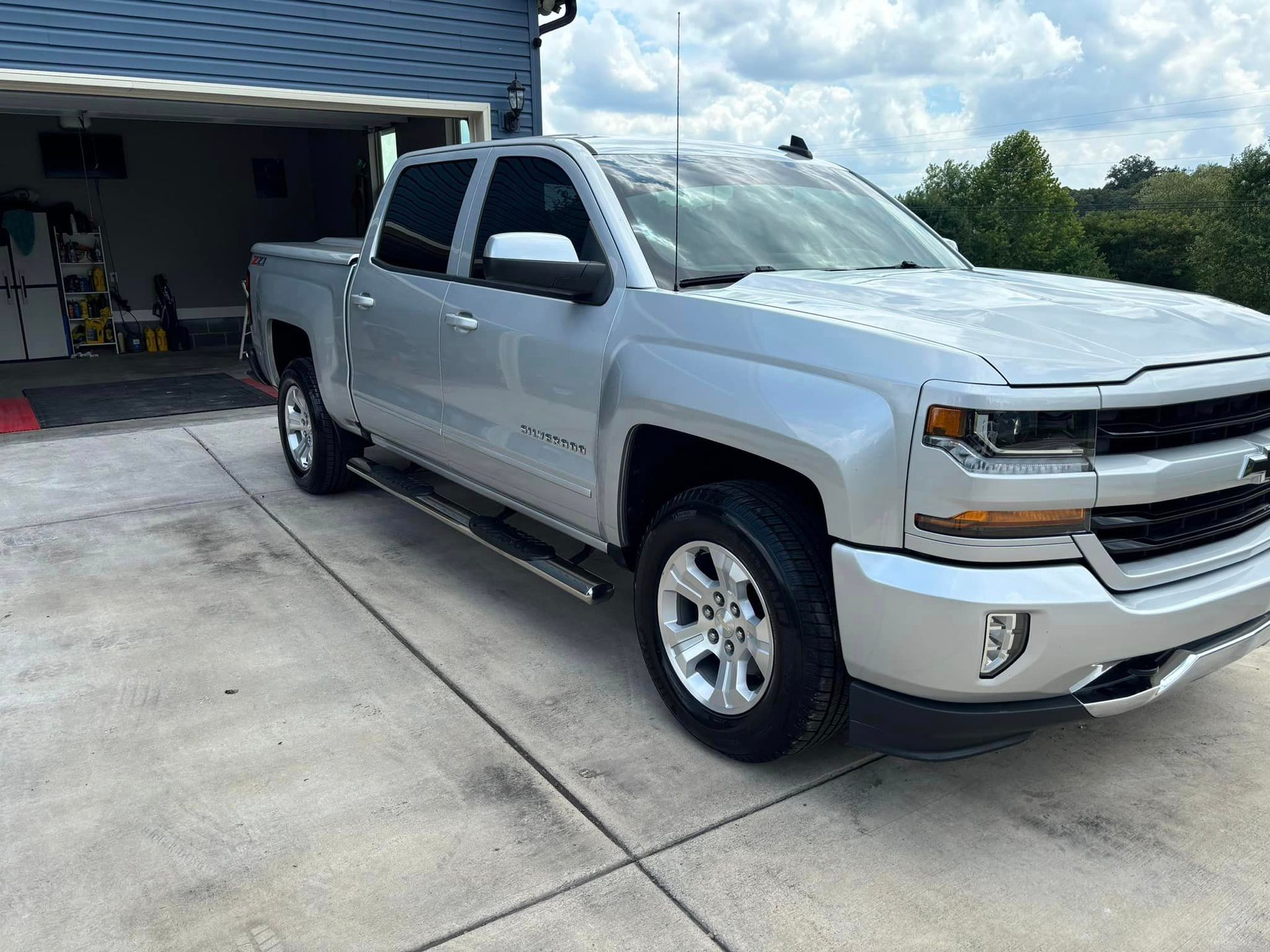 A silver pickup truck is parked in a driveway in front of a garage. A silver pickup truck is parked in a driveway in front of a garage.