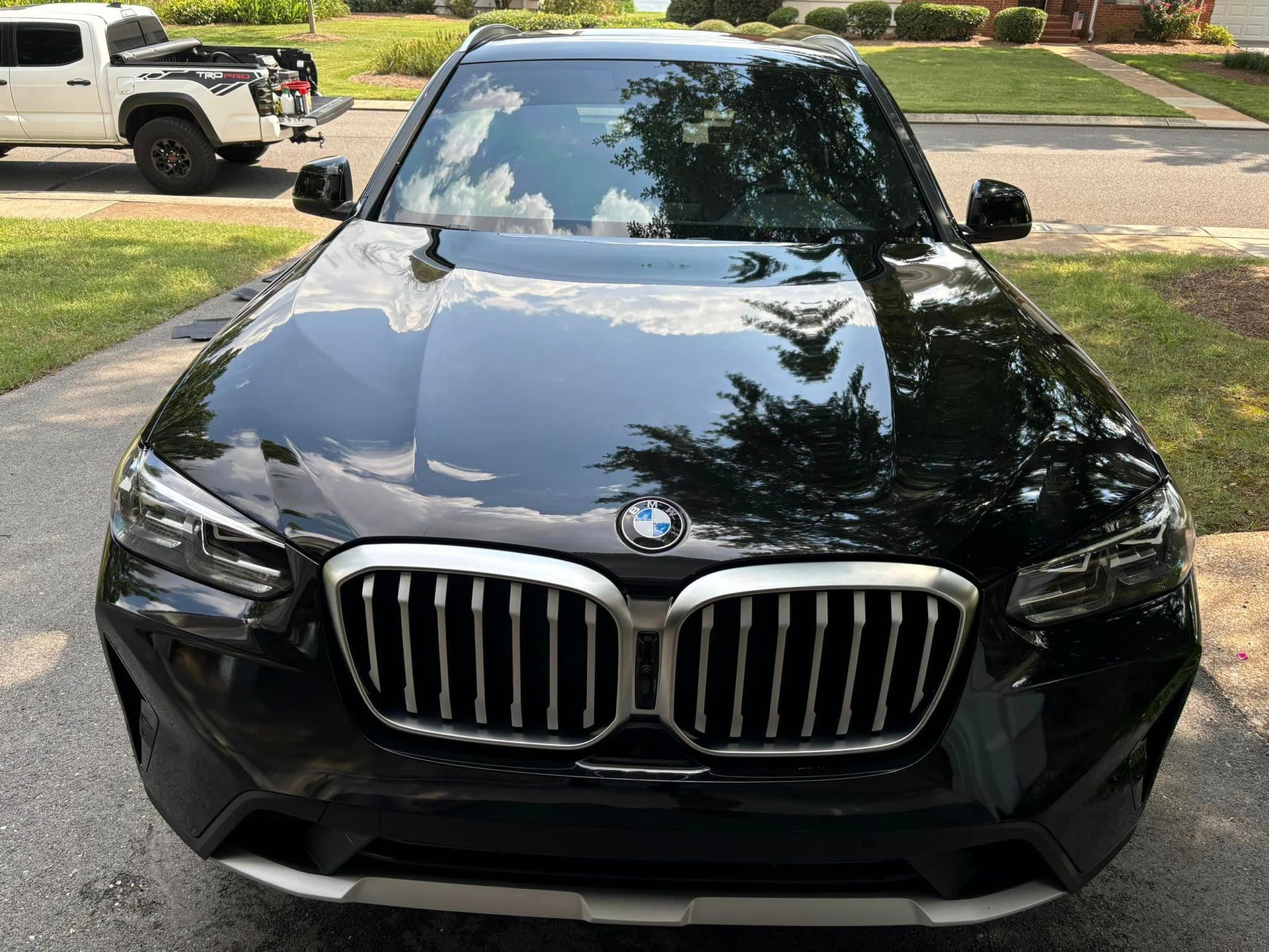 A black bmw x3 is parked in a driveway next to a white truck.