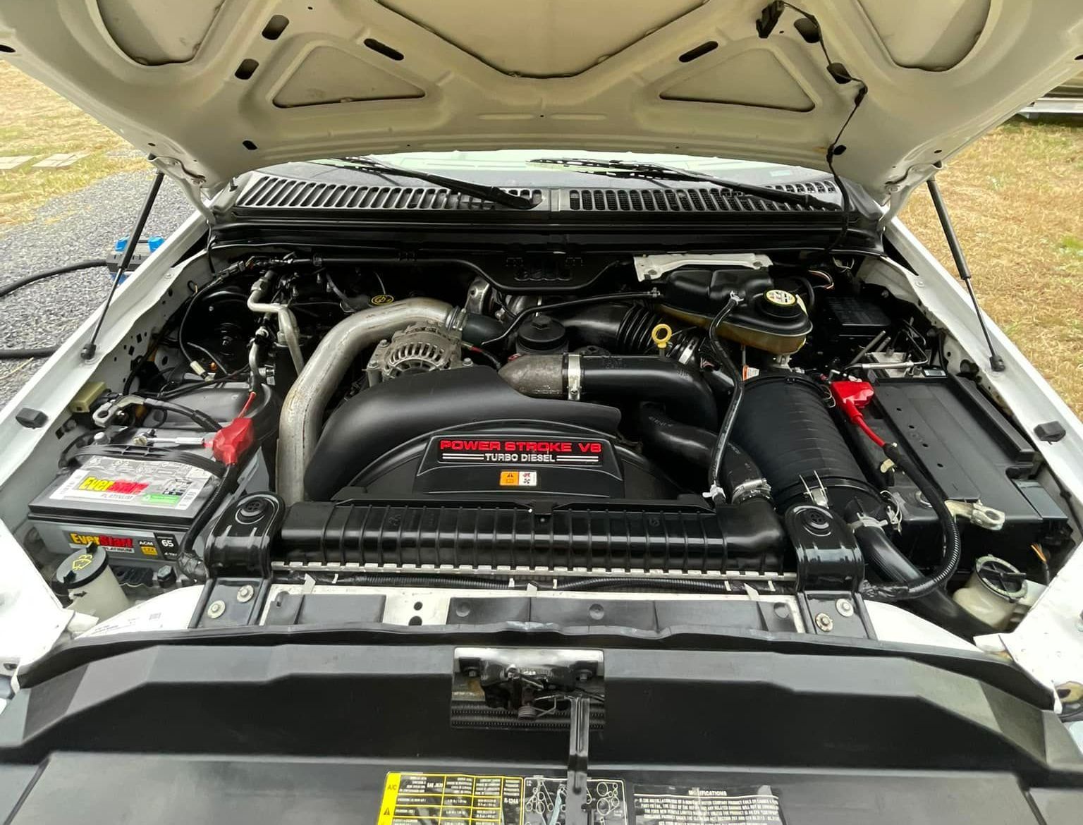 The engine of a silver truck is shown with the hood open.
