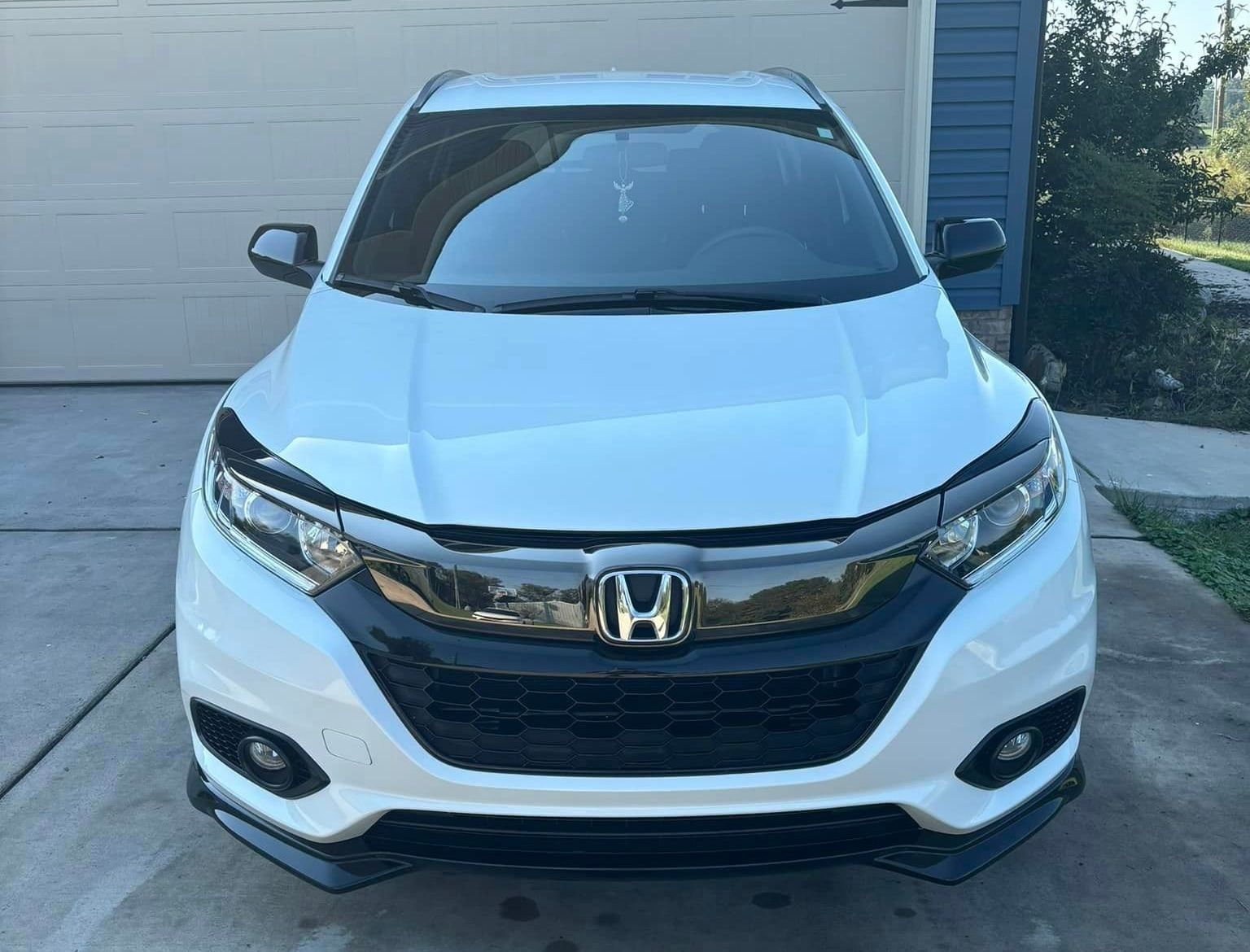 A white honda hrv is parked in front of a garage door.