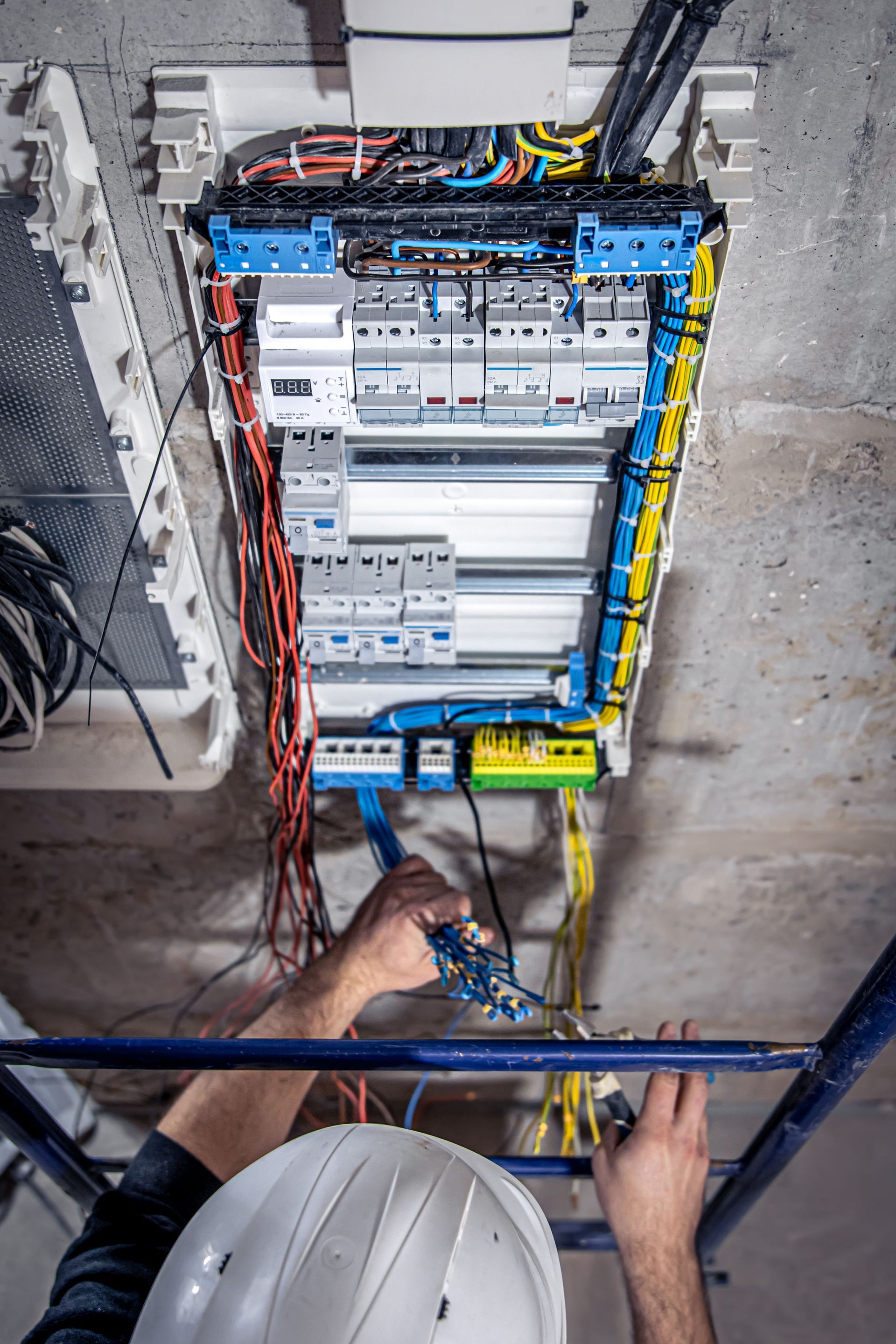 A man wearing a hard hat is working on an electrical box.