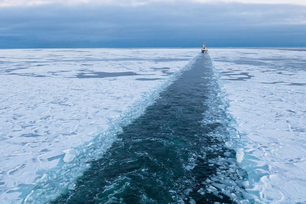 Icebreaker ship carving a path through icy Arctic waters. Blue and white colors dominate scene.