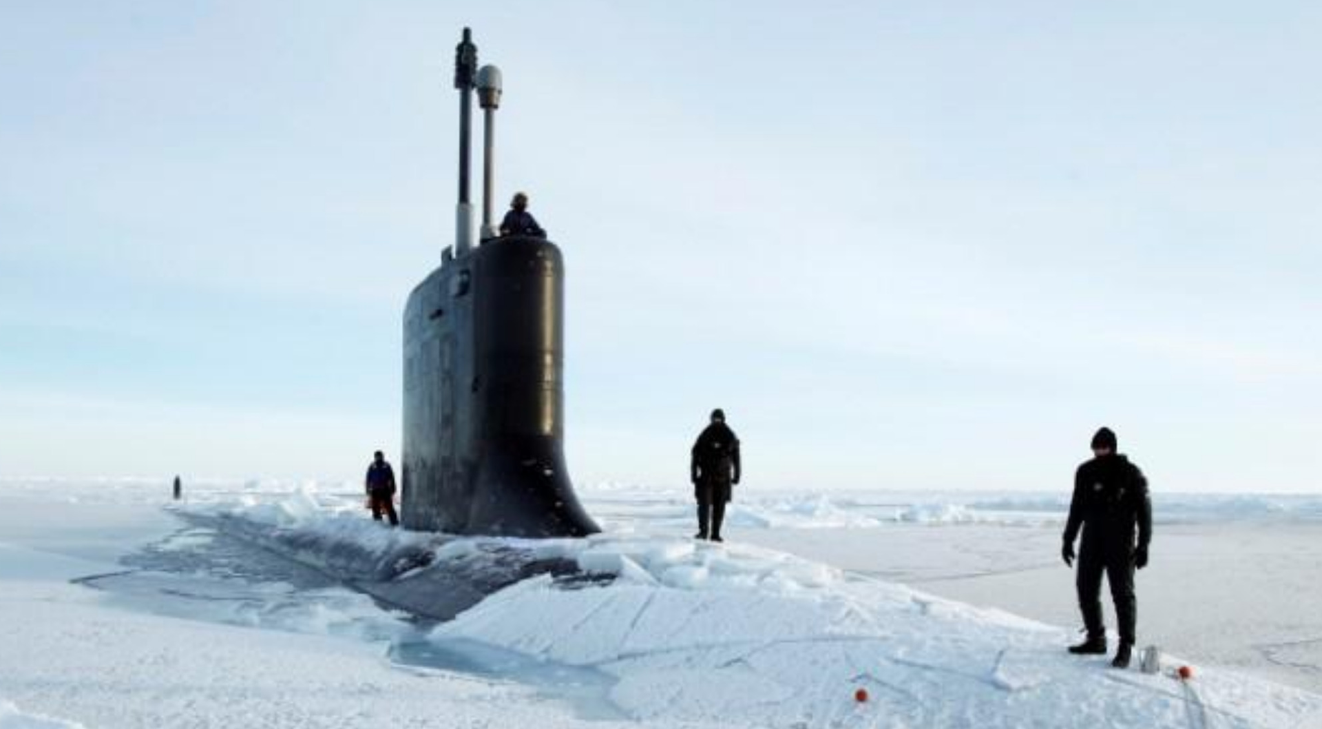 Submarine surfacing through ice, men standing on the deck under a clear sky.