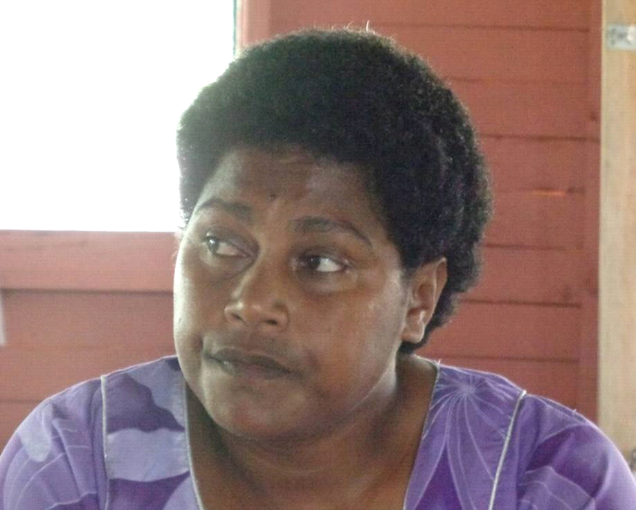 Woman with dark skin, short curly black hair, wearing a purple floral patterned shirt, looking to her right.