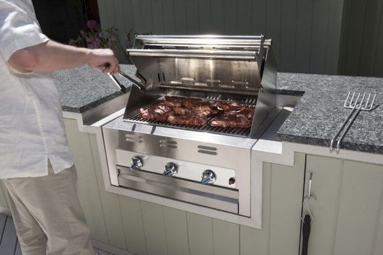 man grilling chicken on stainless steel grill with granite countertop.