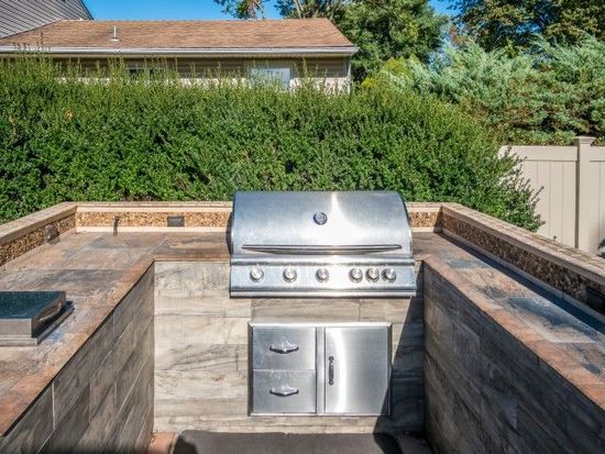stainless steel grill outdoors with brown counter in galley area with bushes behind