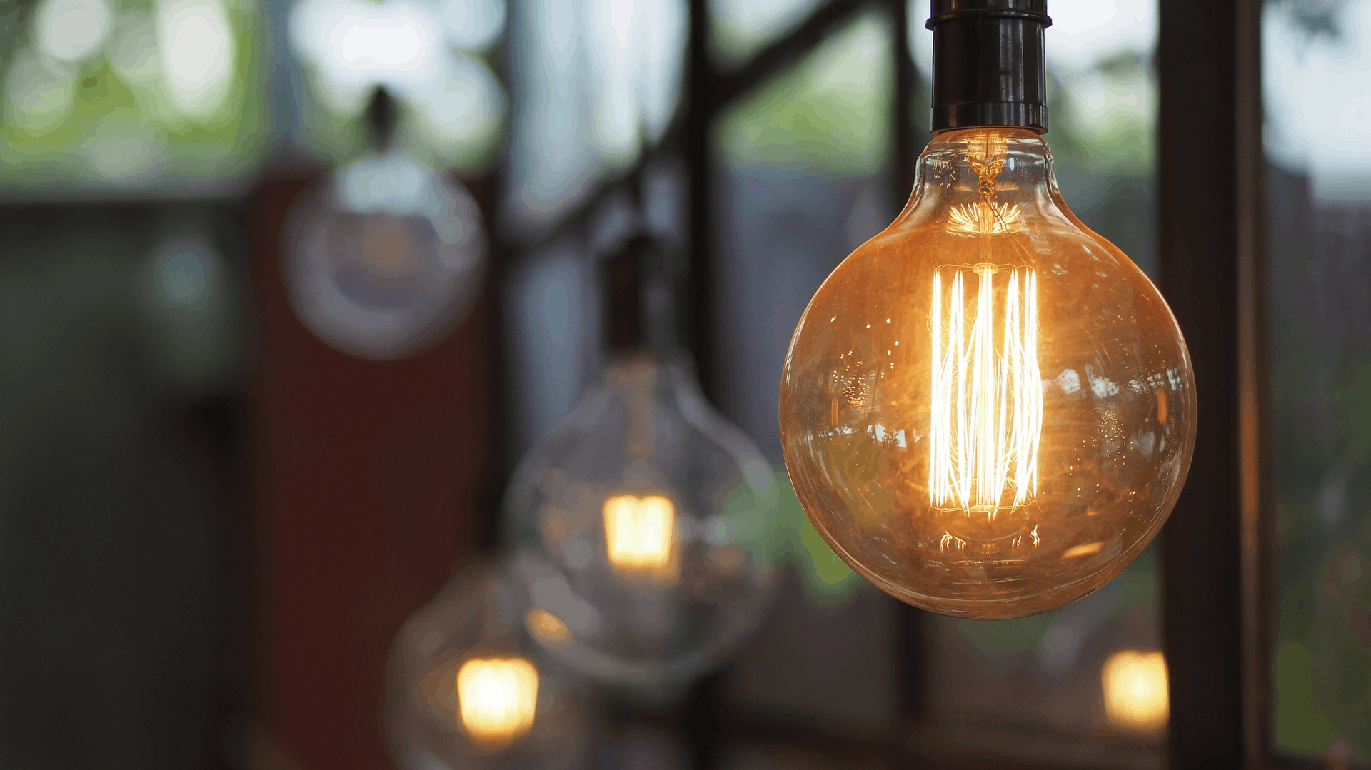 Close-up of a lit, amber-colored Edison bulb hanging from a dark fixture. Other bulbs are slightly out of focus in the background — Elibon Solutions in Garbutt, QLD