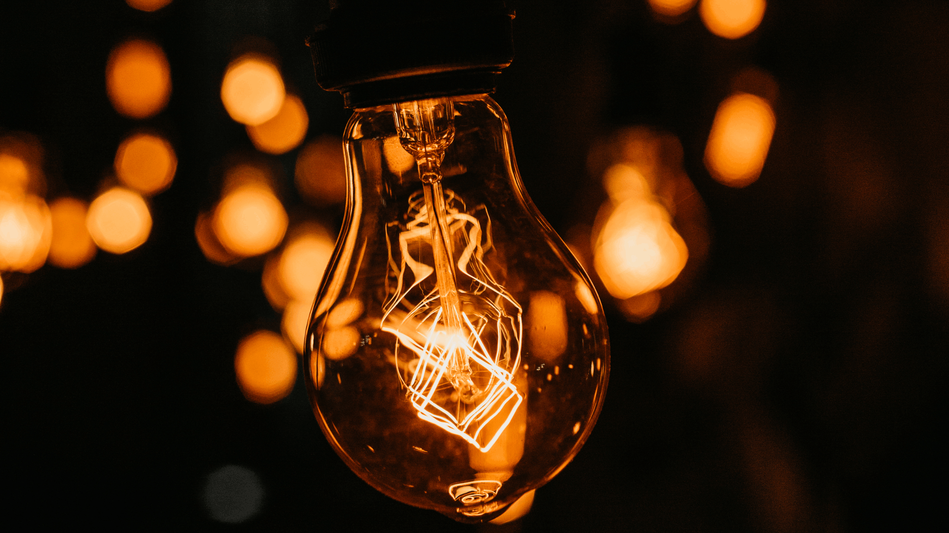 Close-up of a lit lightbulb, with filament glowing, hanging with many other blurred lights, against a dark background — Elibon Solutions in Garbutt, QLD