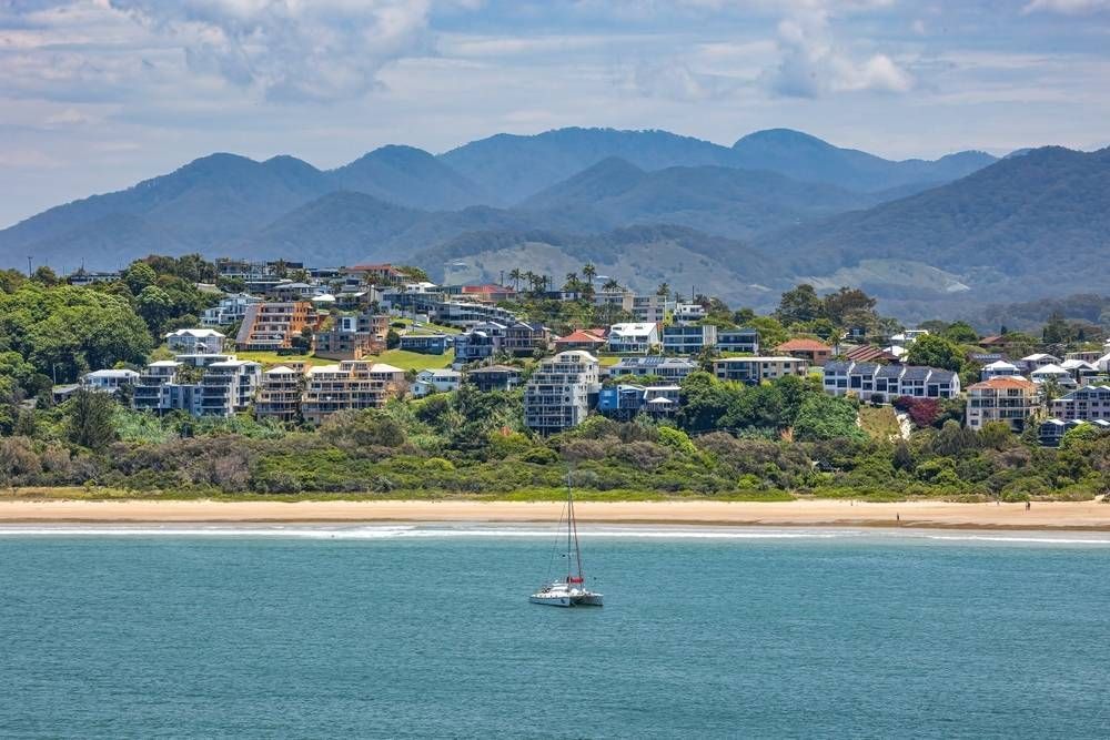 A Sailboat Is Floating On Top Of A Body Of Water With Mountains In The Background — Pegar Transport In Coffs Harbour, NSW